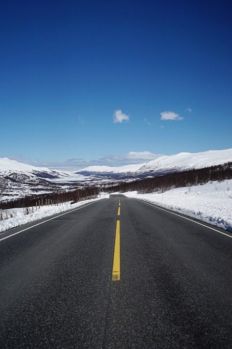 A vertical shot of a road leading to beautiful snowy mountains