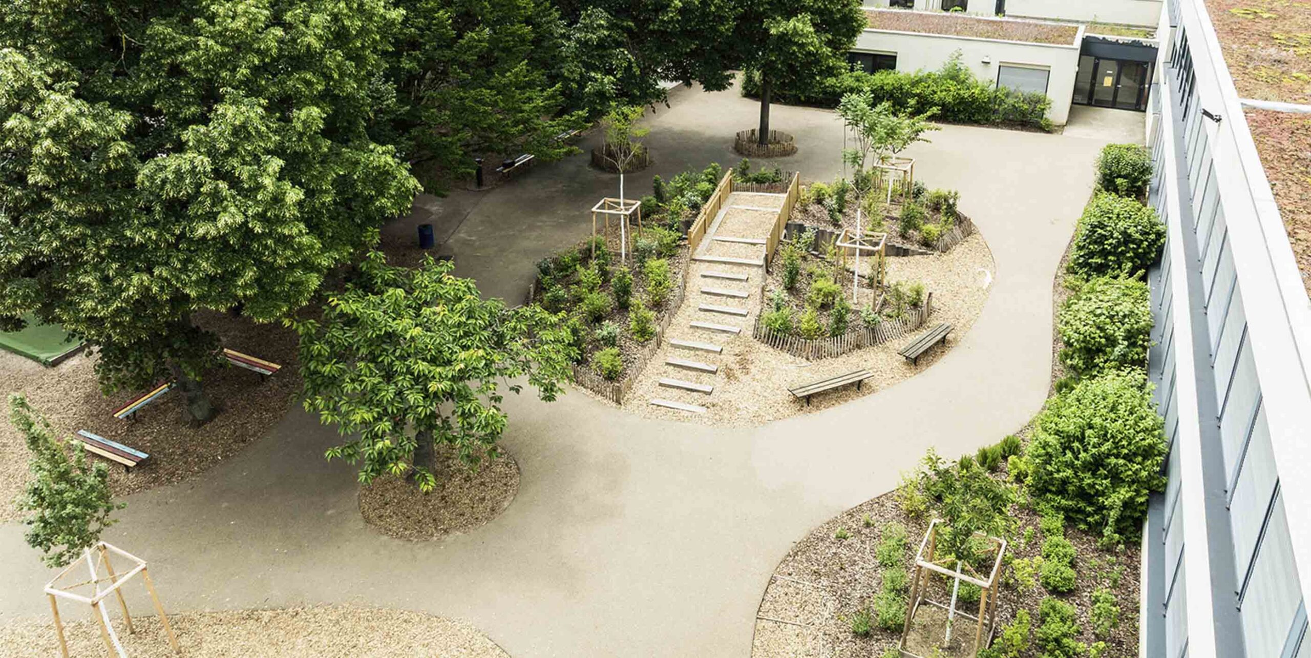 Vue aérienne d'une cour aménagée avec allées, bancs, arbres plantés et massifs végétalisés en gradins.