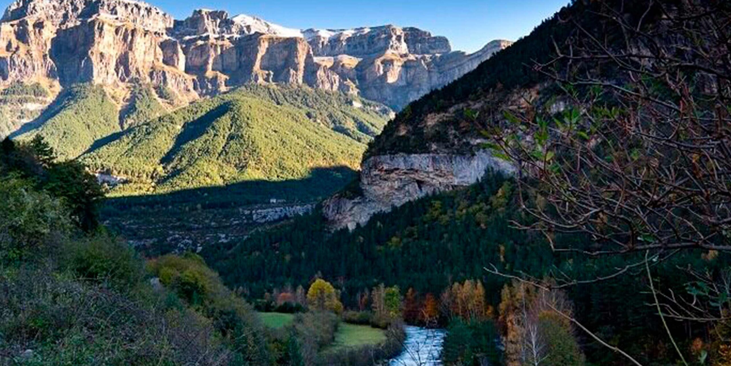 Vallée montagneuse boisée avec falaises rocheuses et rivière en fond de vallée.