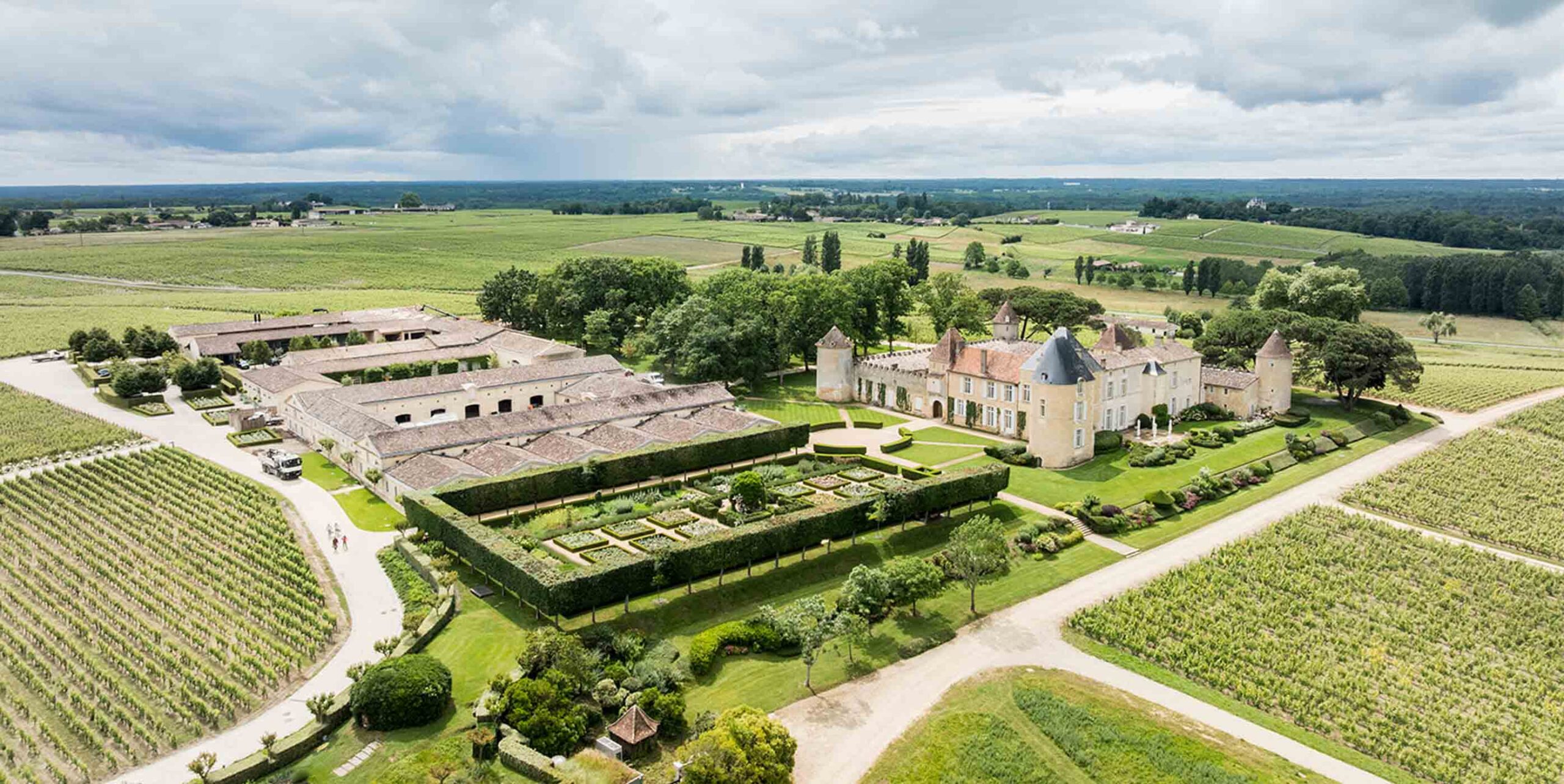 Vue aérienne d'un château entouré de vignobles avec jardins structurés à haies taillées.