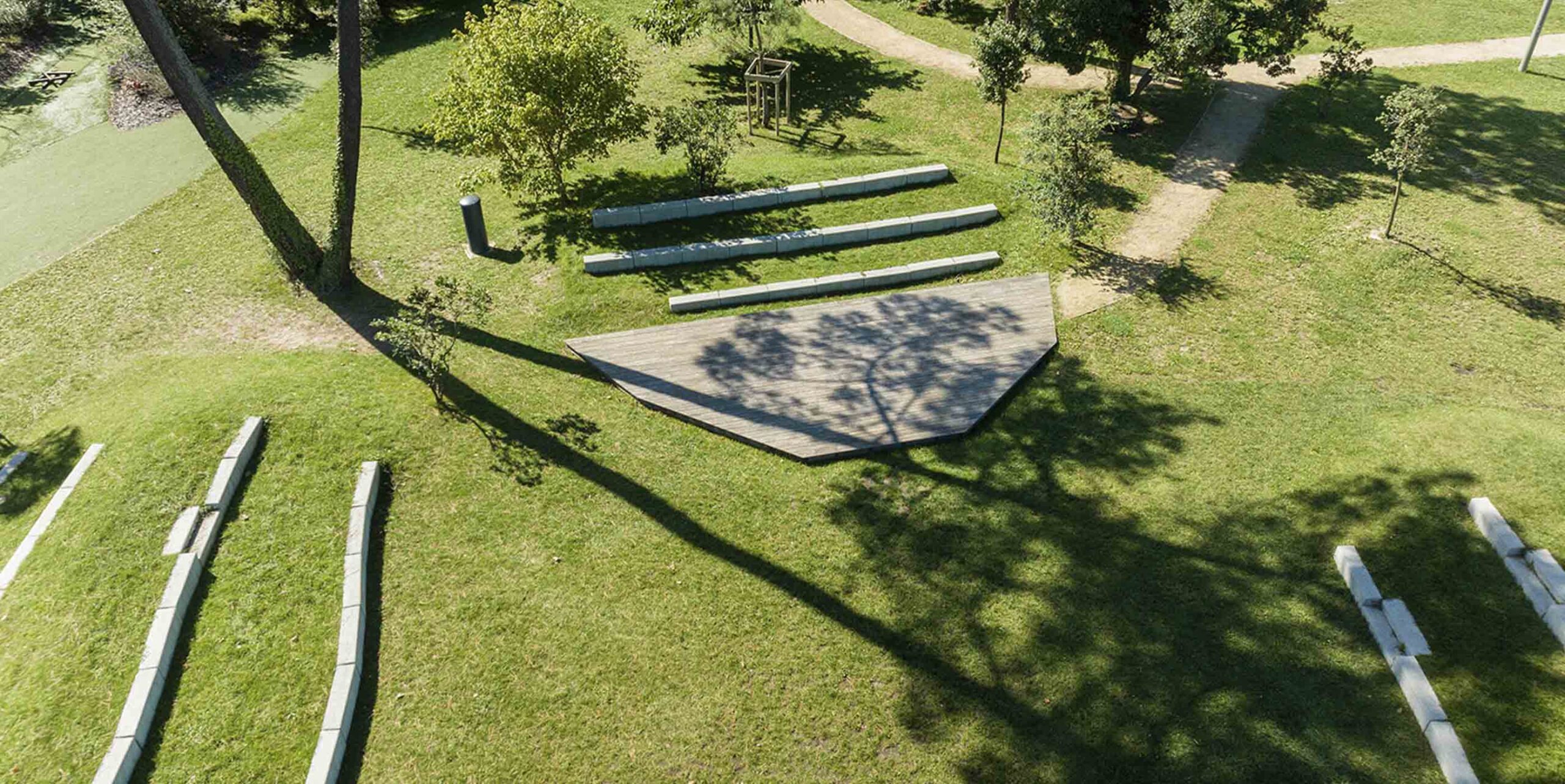 Vue aérienne d'un parc paysager avec pelouse entretenue, arbres, allées et plateforme en bois.