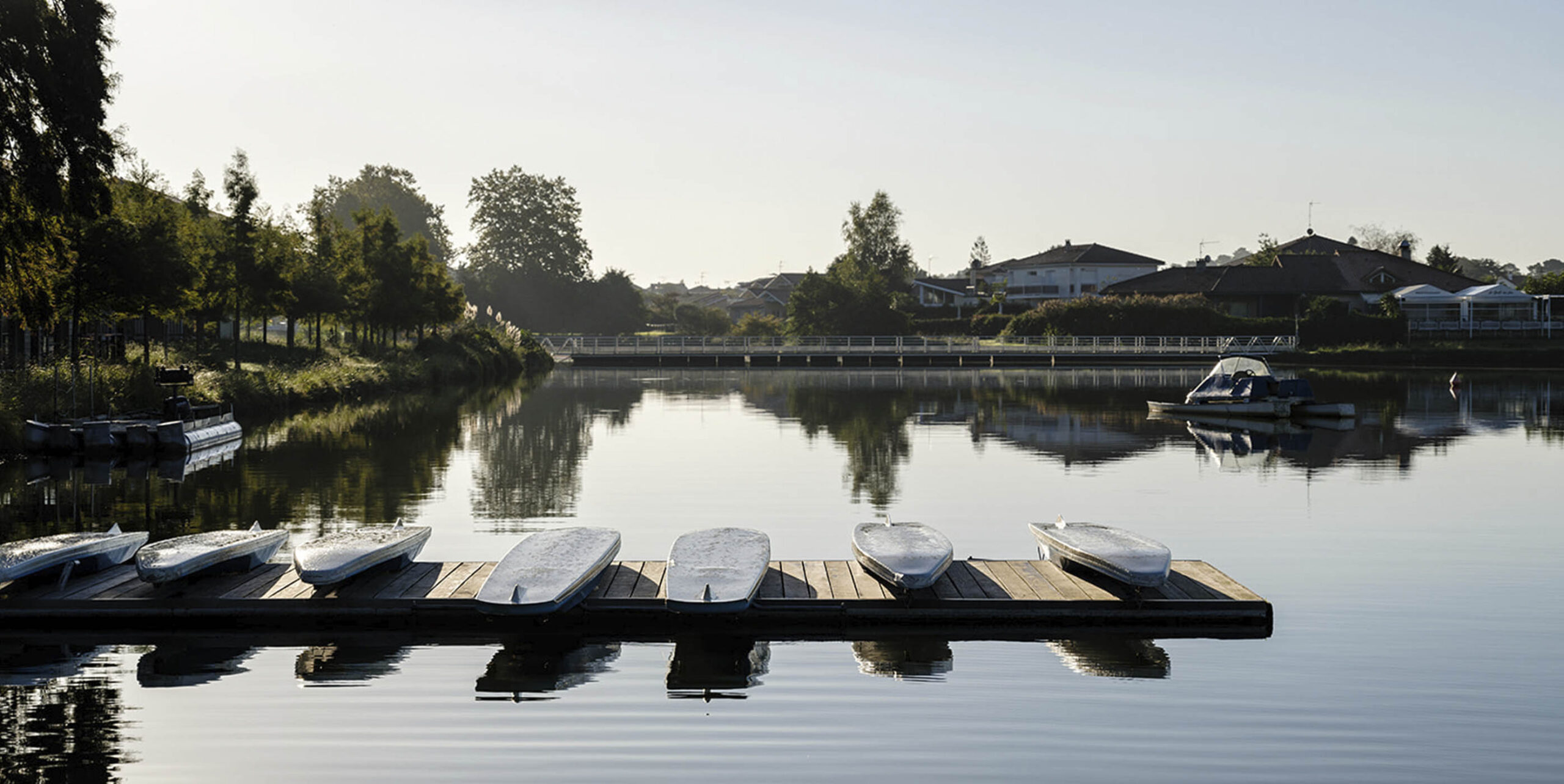 Ponton en bois avec barques retournées sur un plan d'eau bordé d'arbres.