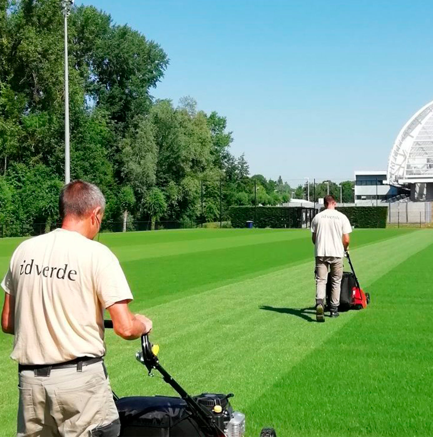Deux agents idverde tondent des terrains de sport à proximité d'un stade.