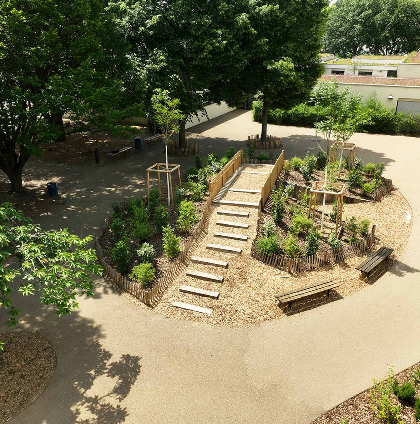 Vue aérienne d'un jardin paysager avec massif surélevé, escalier en bois et bancs intégrés dans une cour arborée.