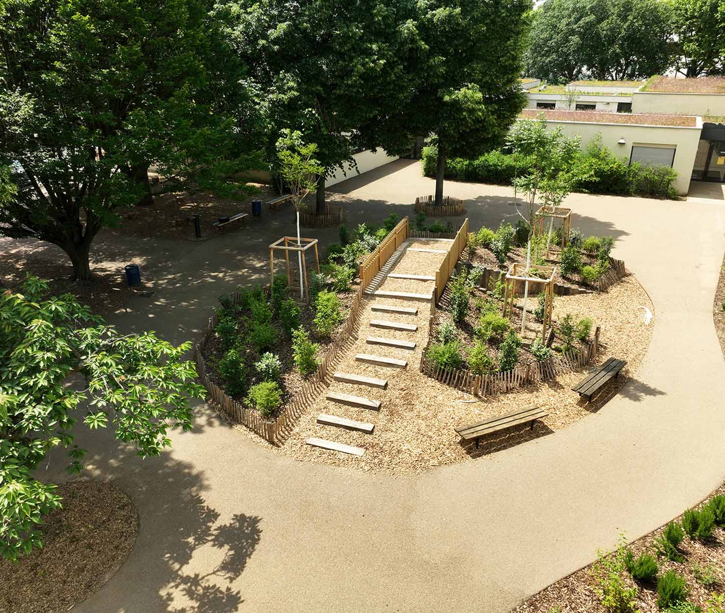 Vue aérienne d'un jardin paysager avec massif surélevé, escalier en bois et bancs intégrés dans une cour arborée.