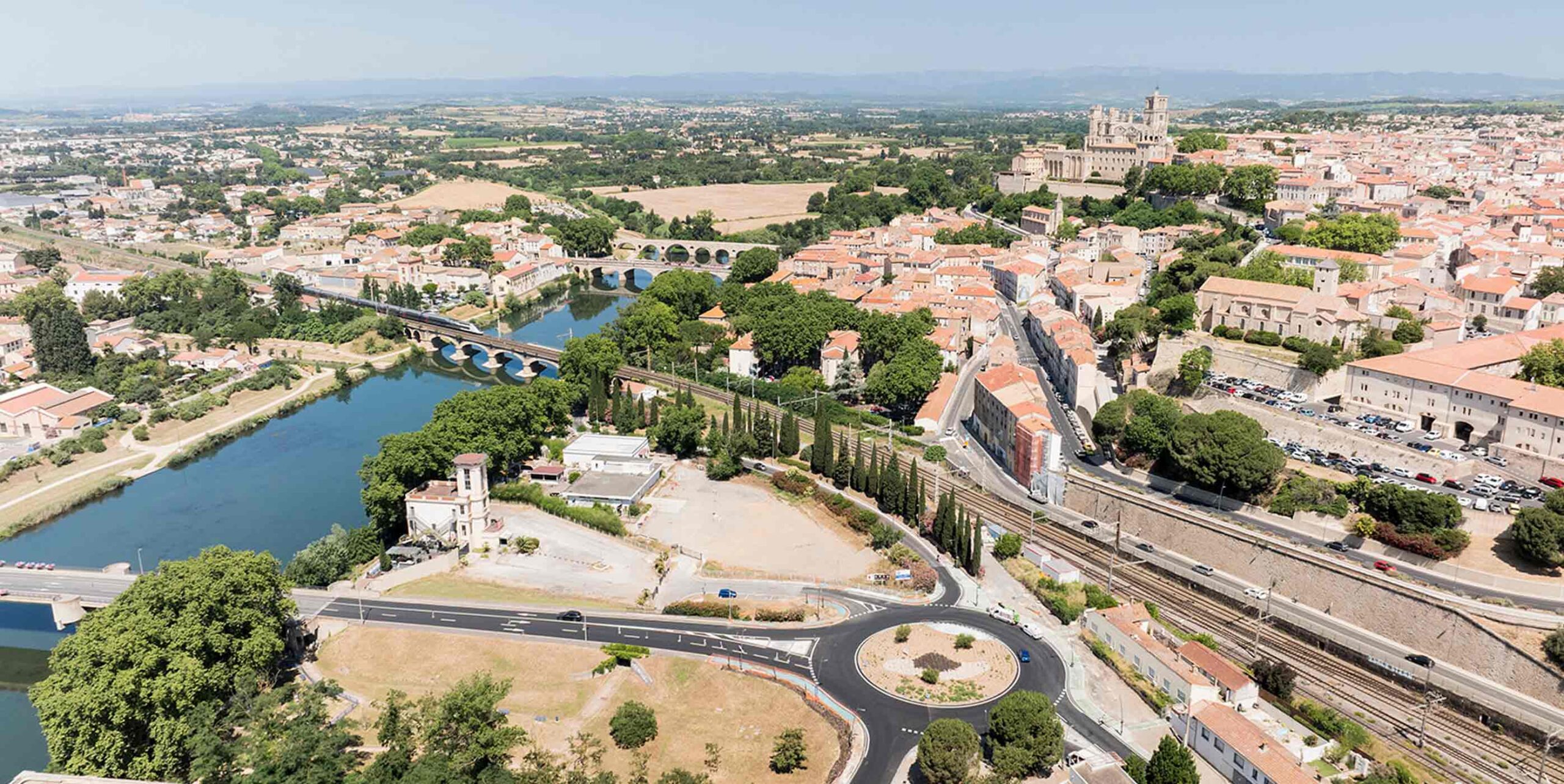 Vue aérienne d'une ville traversée par une rivière, avec ponts, voie ferrée et espaces verts urbains.