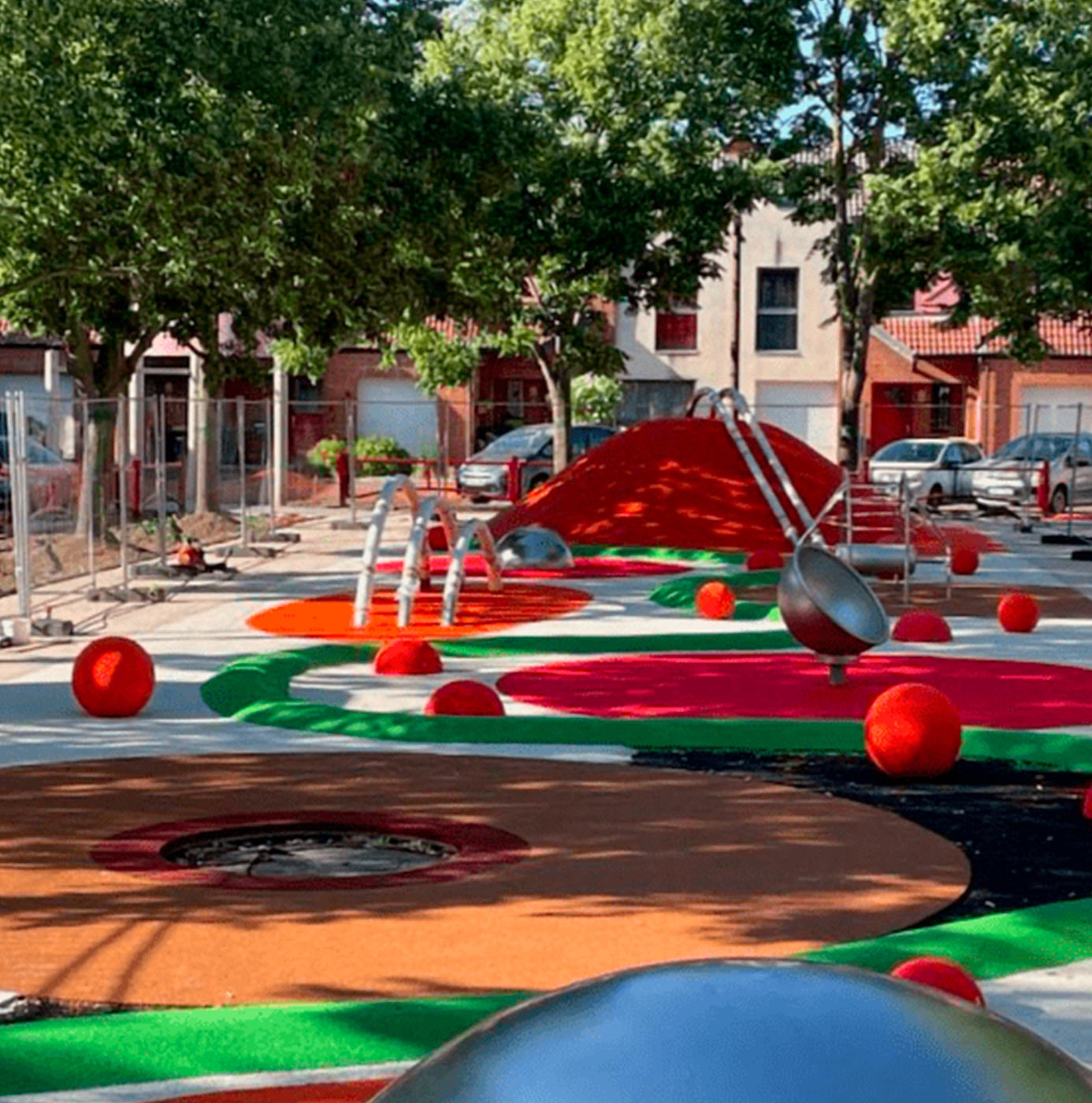 Aire de jeux au sol multicolore avec structures en forme de sphères rouges et toboggan.