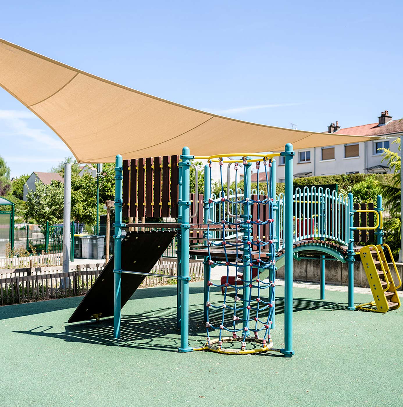Aire de jeux avec structure d'escalade, toboggan et voile d'ombrage installée dans un espace public.
