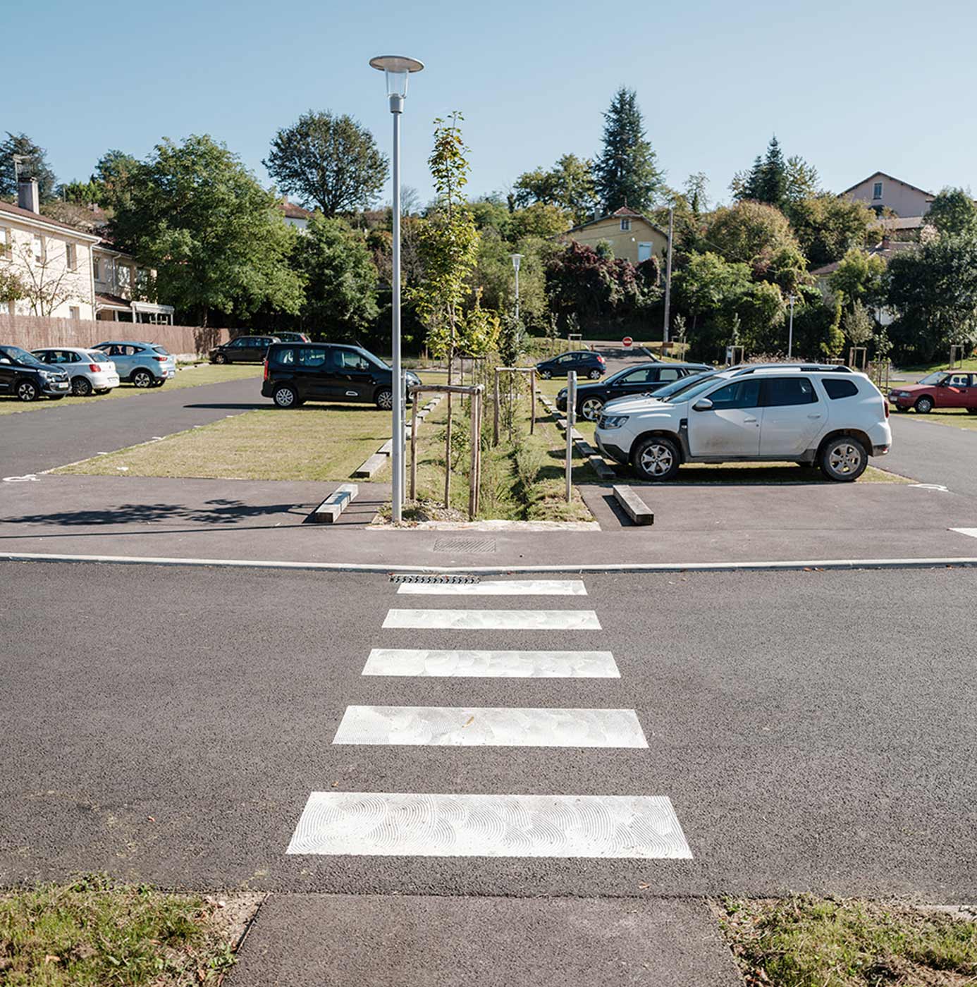 Parking paysager avec bandes végétalisées plantées de jeunes arbres, séparant les rangées de stationnement.