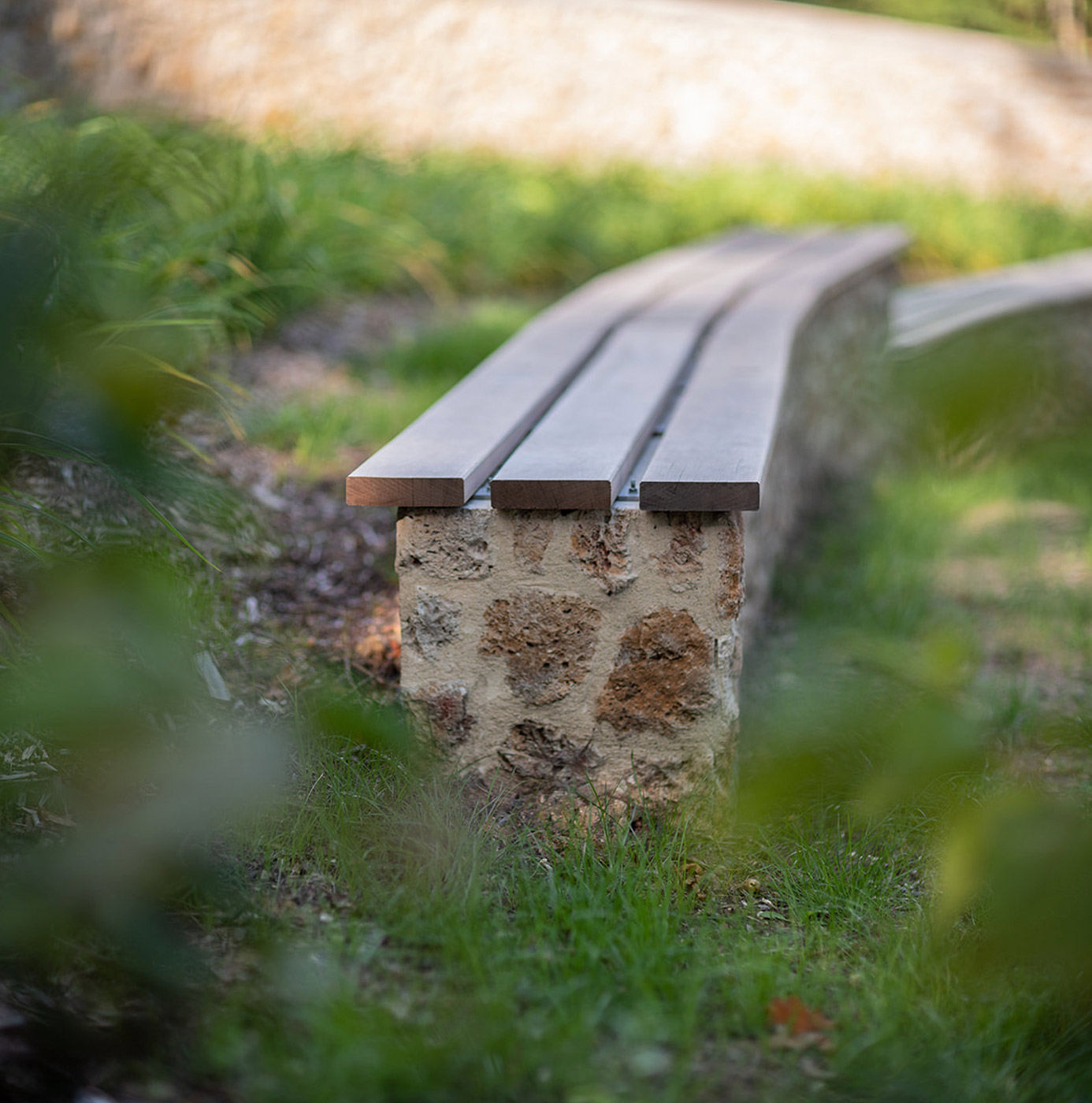 Banc en bois à lattes reposant sur un socle en pierre, installé dans un espace vert engazonné.