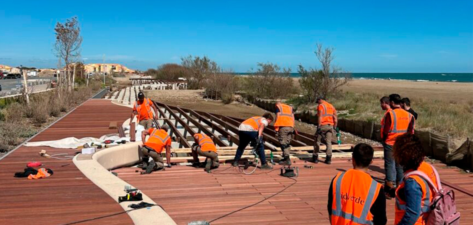 Des agents idverde installent une passerelle en bois sur un platelage de bord de mer.