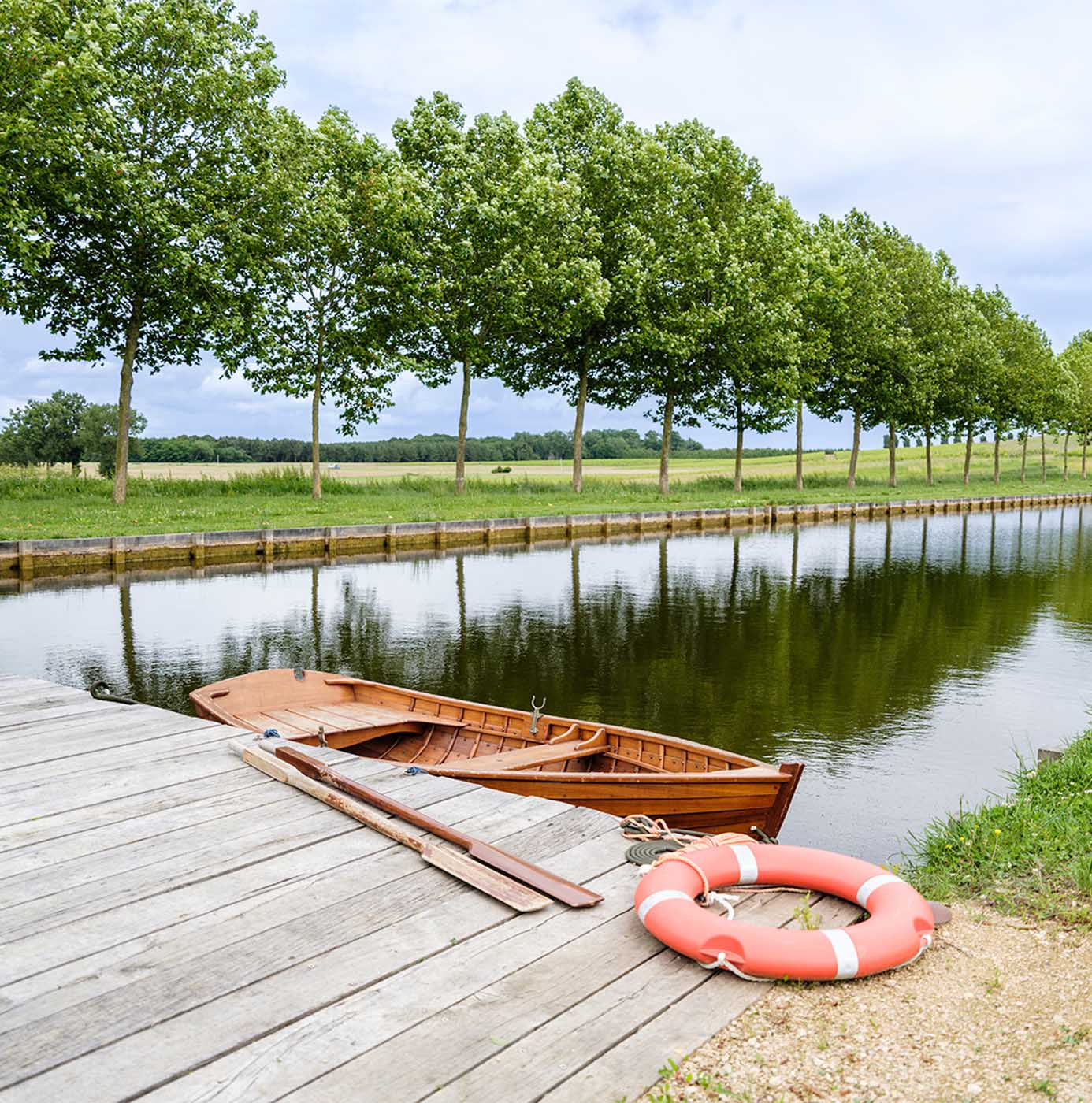 Barque en bois amarrée le long d'un canal bordé d'un alignement d'arbres.