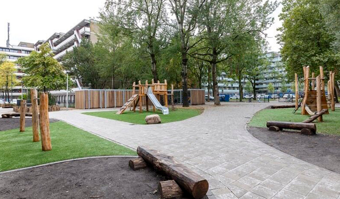 Aire de jeux paysagère en pied d'immeubles avec toboggan en bois, structure de grimpe et cheminements minéraux.