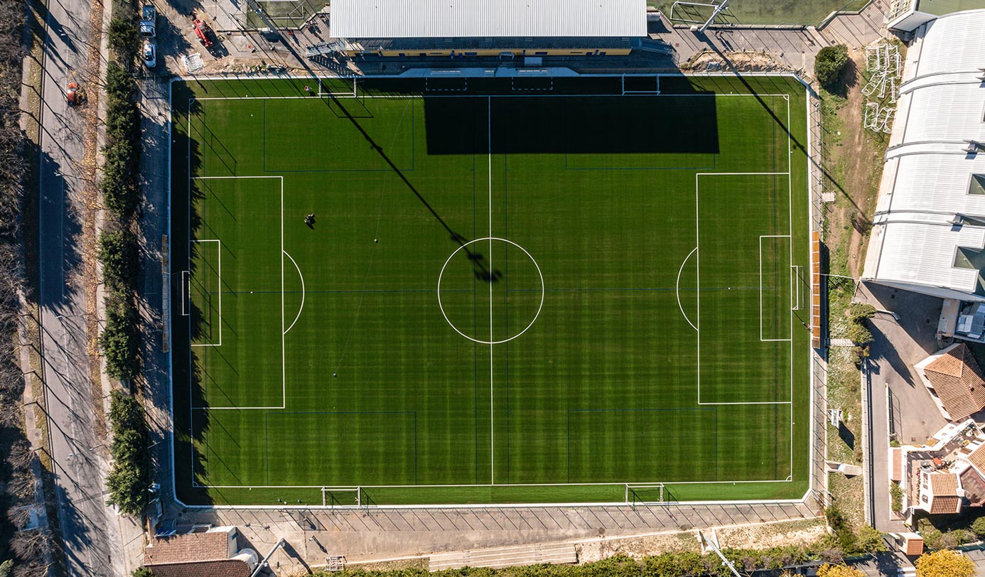 Vue aérienne d'un terrain de football entretenu, avec un agent tondant la pelouse.