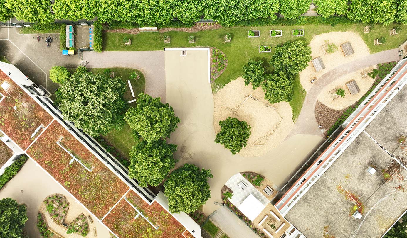 Vue aérienne d'un espace vert résidentiel avec aire de jeux, allées et bandes plantées entre deux bâtiments.