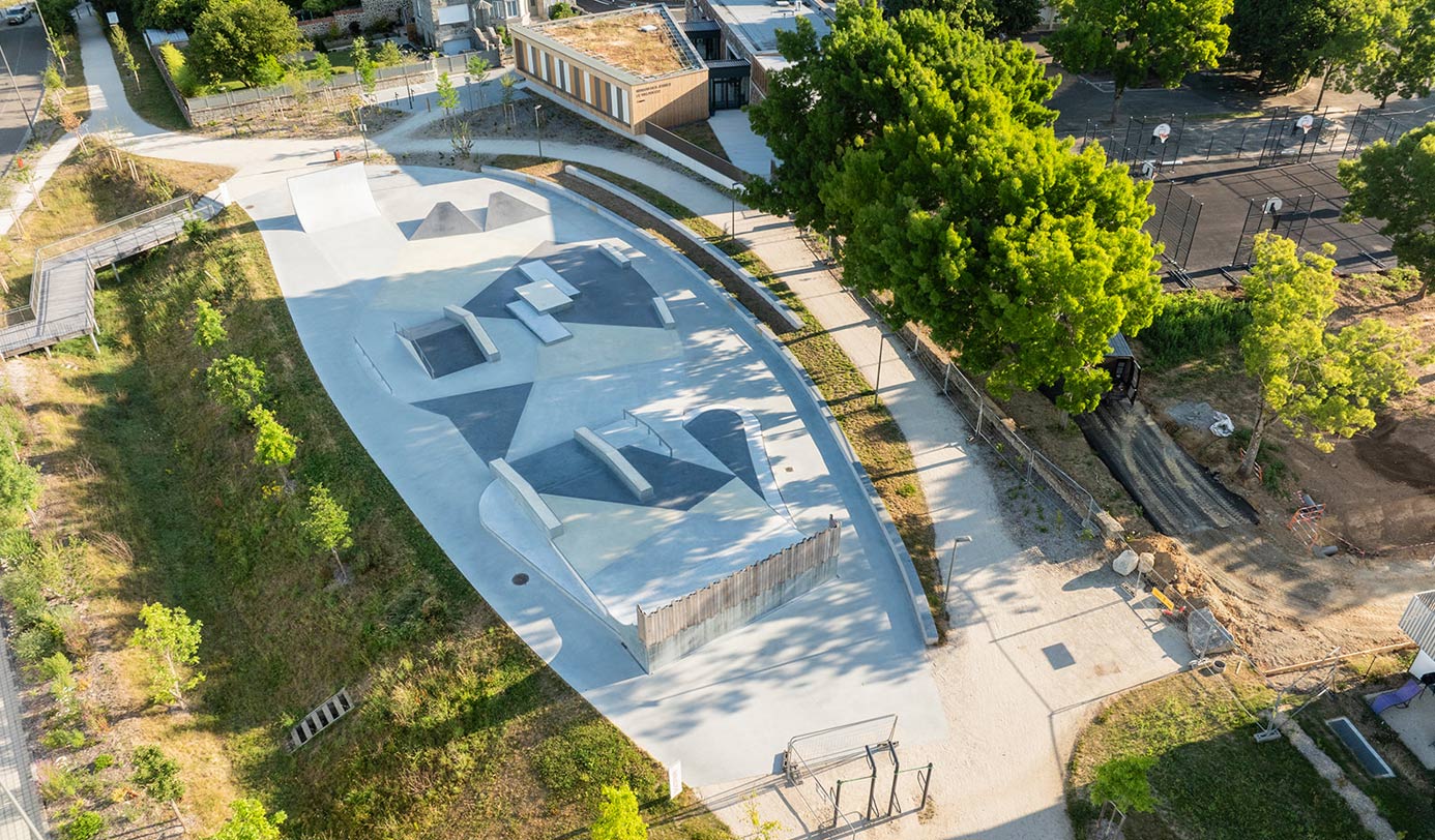 Vue aérienne d'un skatepark aménagé au sein d'un parc urbain, entouré d'espaces verts et d'arbres.