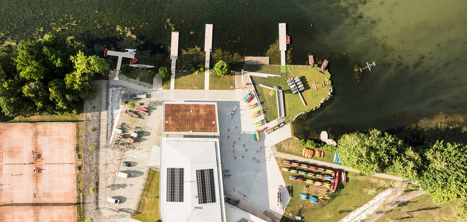 Vue aérienne d'une base nautique avec pontons, kayaks et espaces verts aménagés en bord de plan d'eau.