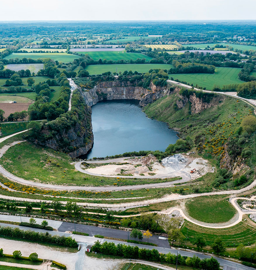 Vue aérienne d'une ancienne carrière reconvertie en plan d'eau entouré de falaises végétalisées et de paysages ruraux.