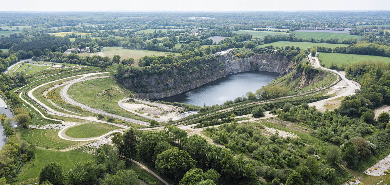 Vue aérienne d'une ancienne carrière réaménagée en espace paysager avec plan d'eau, chemins et plantations.