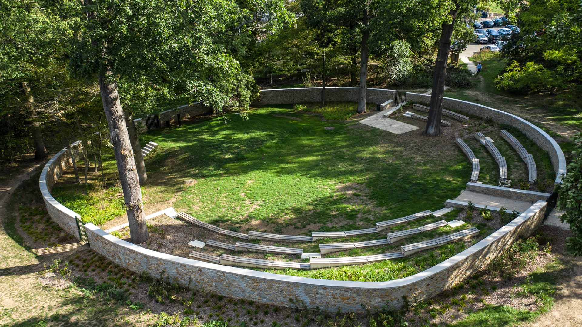 Amphithéâtre de plein air circulaire en pierre avec gradins et pelouse centrale, entouré d'arbres