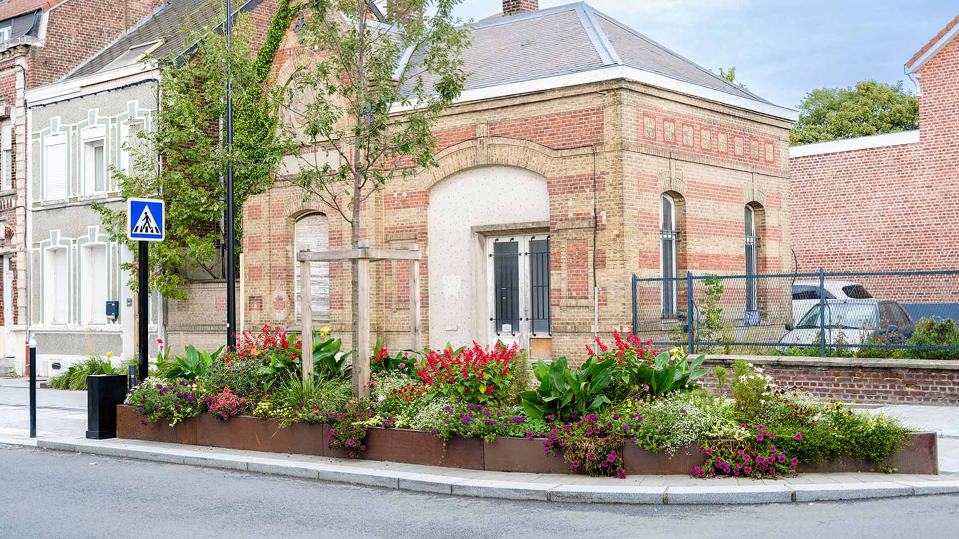 Massif fleuri coloré devant un bâtiment en briques rouges et beiges dans une rue française