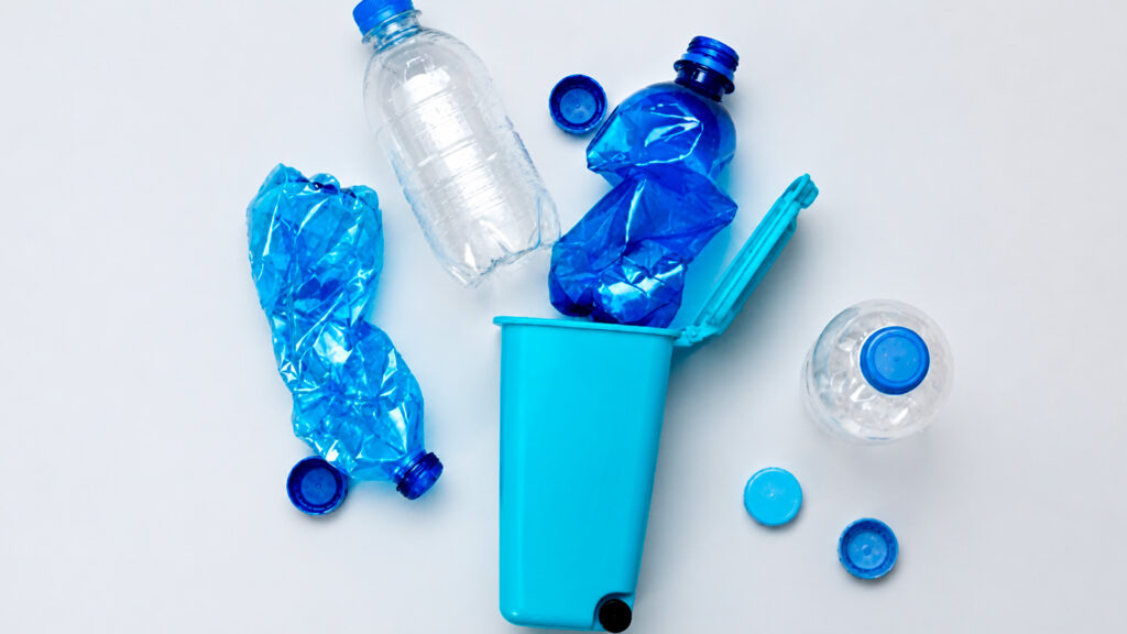 Bouteilles en plastique froissées et capsules bleues éparpillées autour d'une poubelle de recyclage turquoise