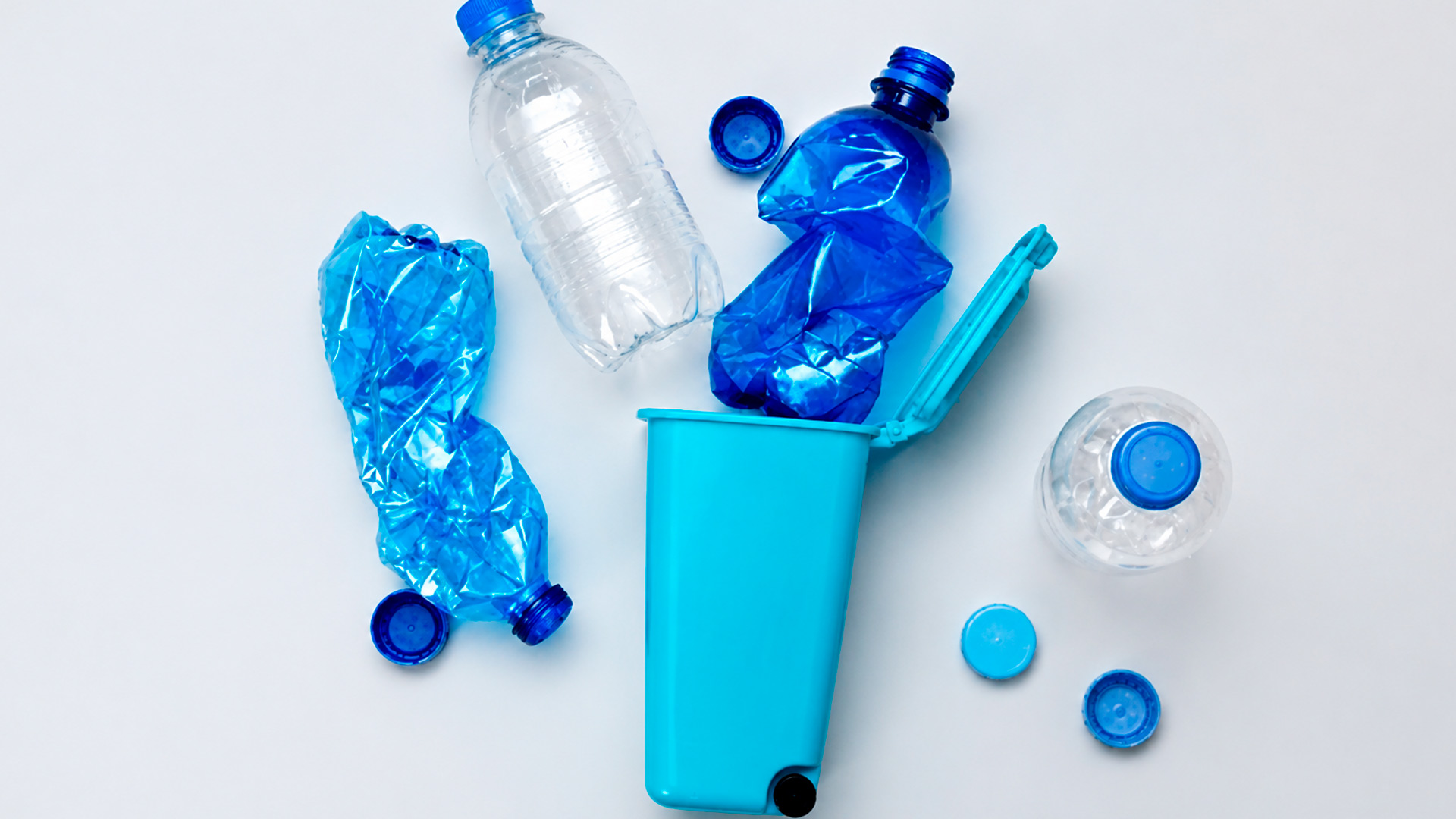 Bouteilles en plastique froissées et capsules bleues éparpillées autour d'une poubelle de recyclage turquoise