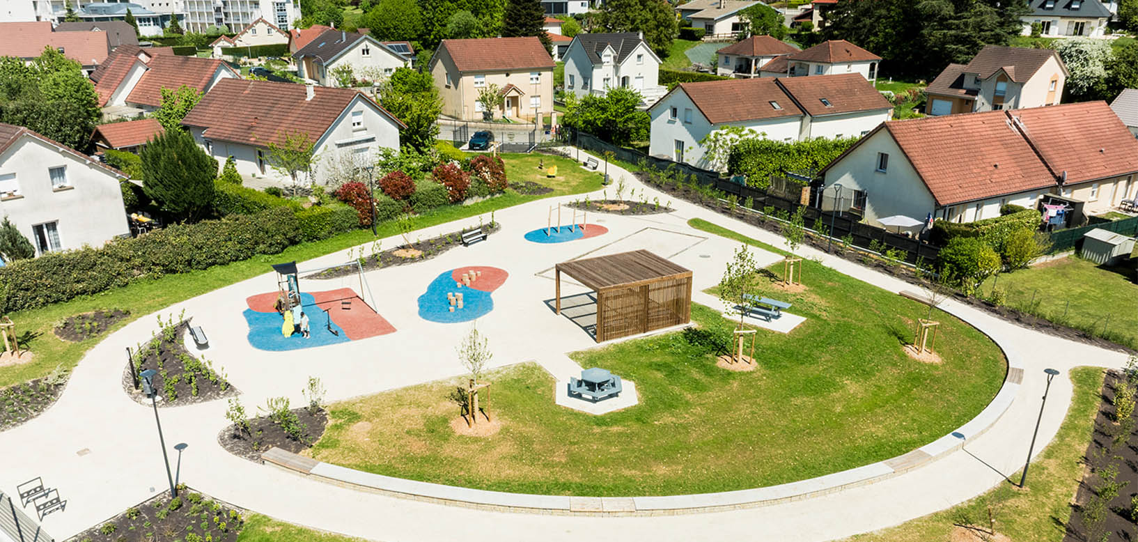 Vue aérienne d'un parc paysager avec aire de jeux, pergola en bois et pelouses aménagées en zone résidentielle.