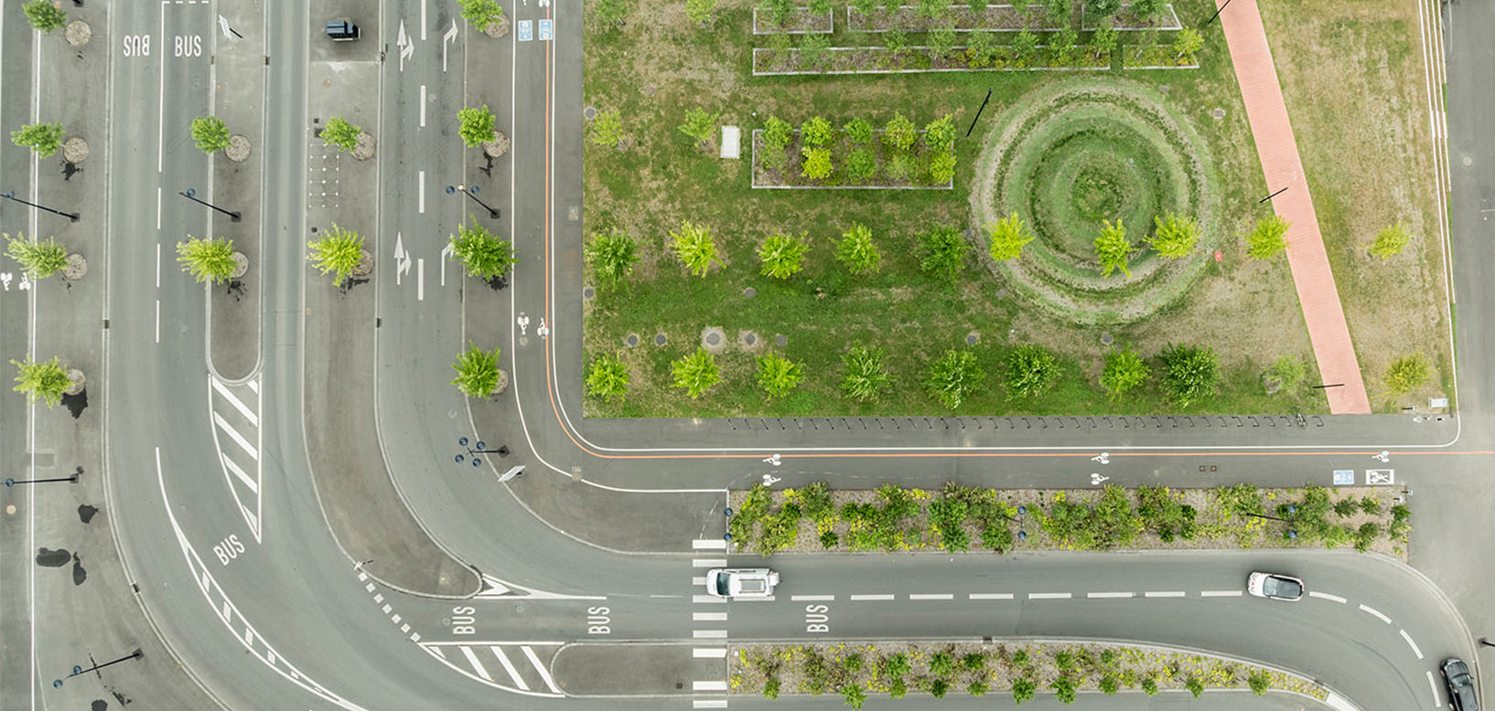 Vue aérienne d'un aménagement paysager urbain en carrefour, avec massifs arbustifs, pelouse circulaire et allée piétonne.