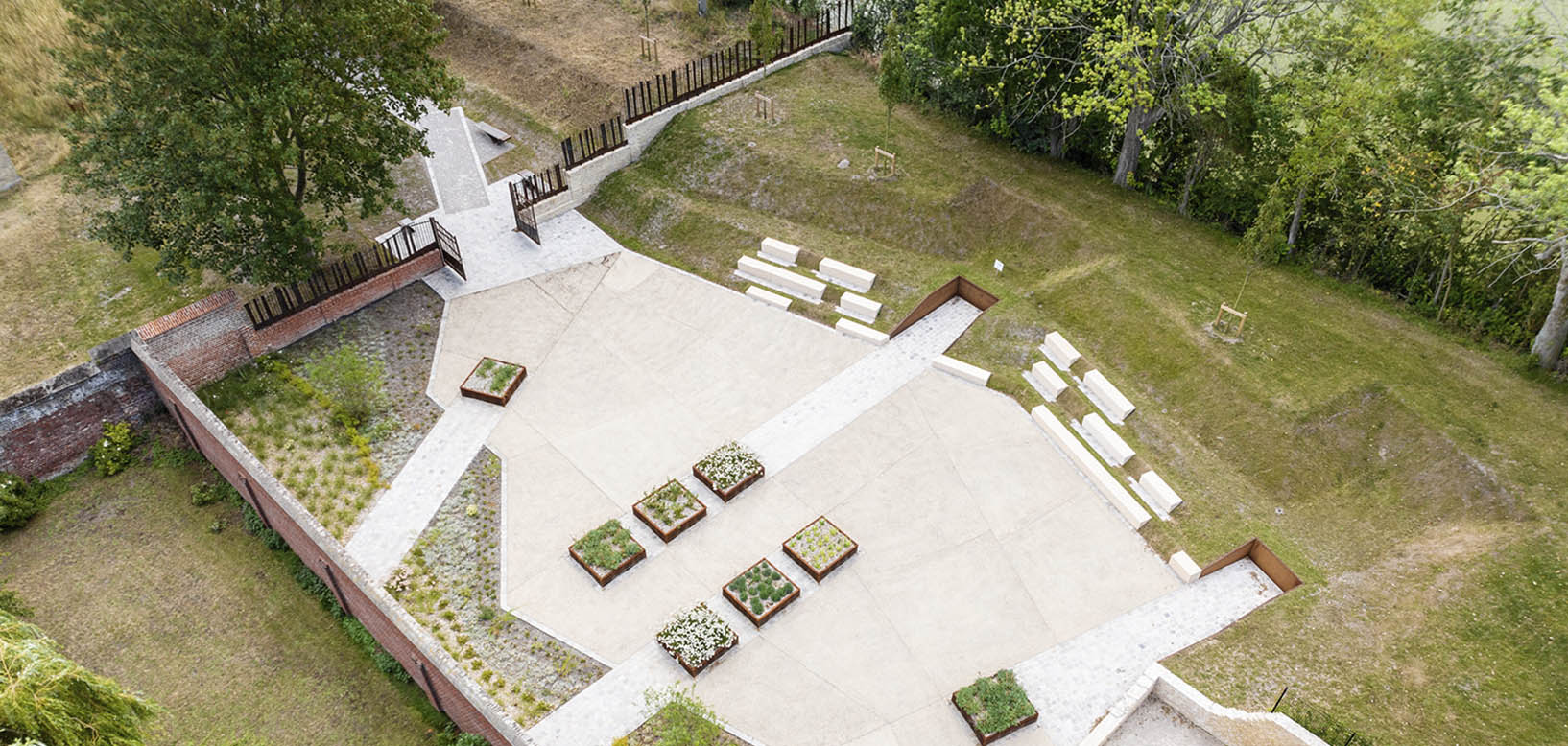 Vue aérienne d'un aménagement paysager avec esplanade minérale, bacs de plantation et pelouses.