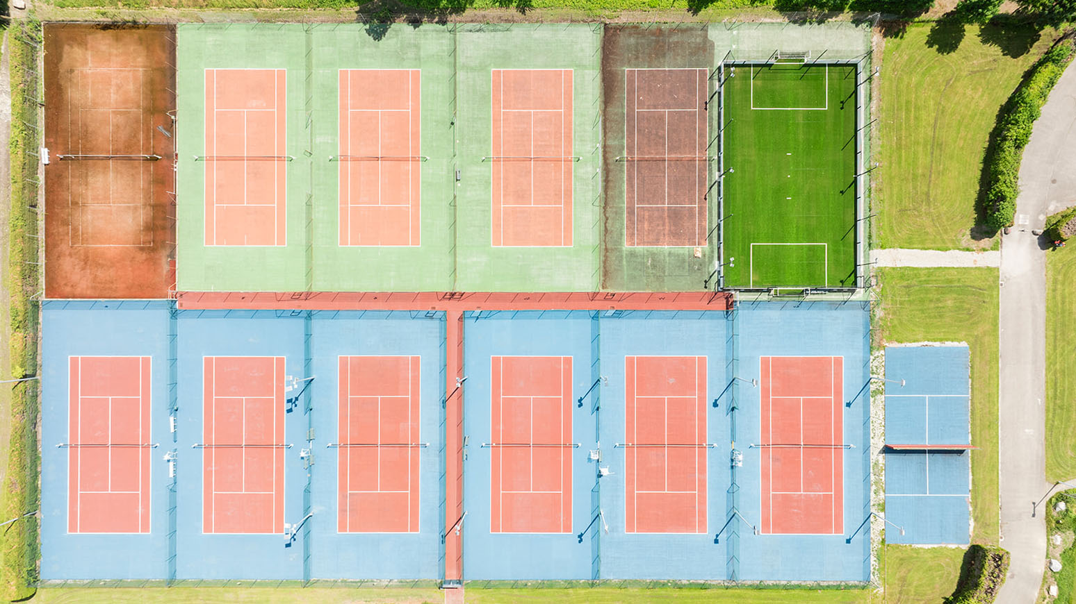Vue aérienne de courts de tennis aux surfaces variées : terre battue, résine bleue et gazon synthétique