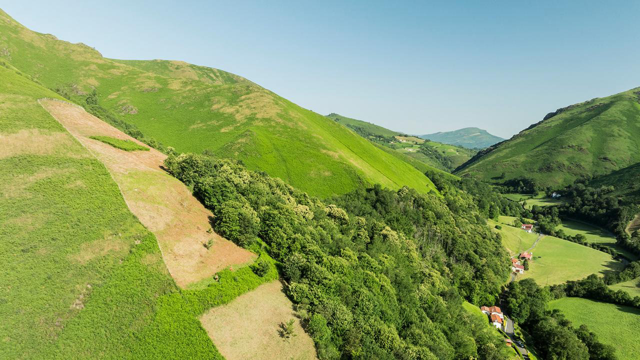 Vue aérienne d'une vallée verdoyante avec collines, forêts et maisons à toits rouges dans un parc naturel français