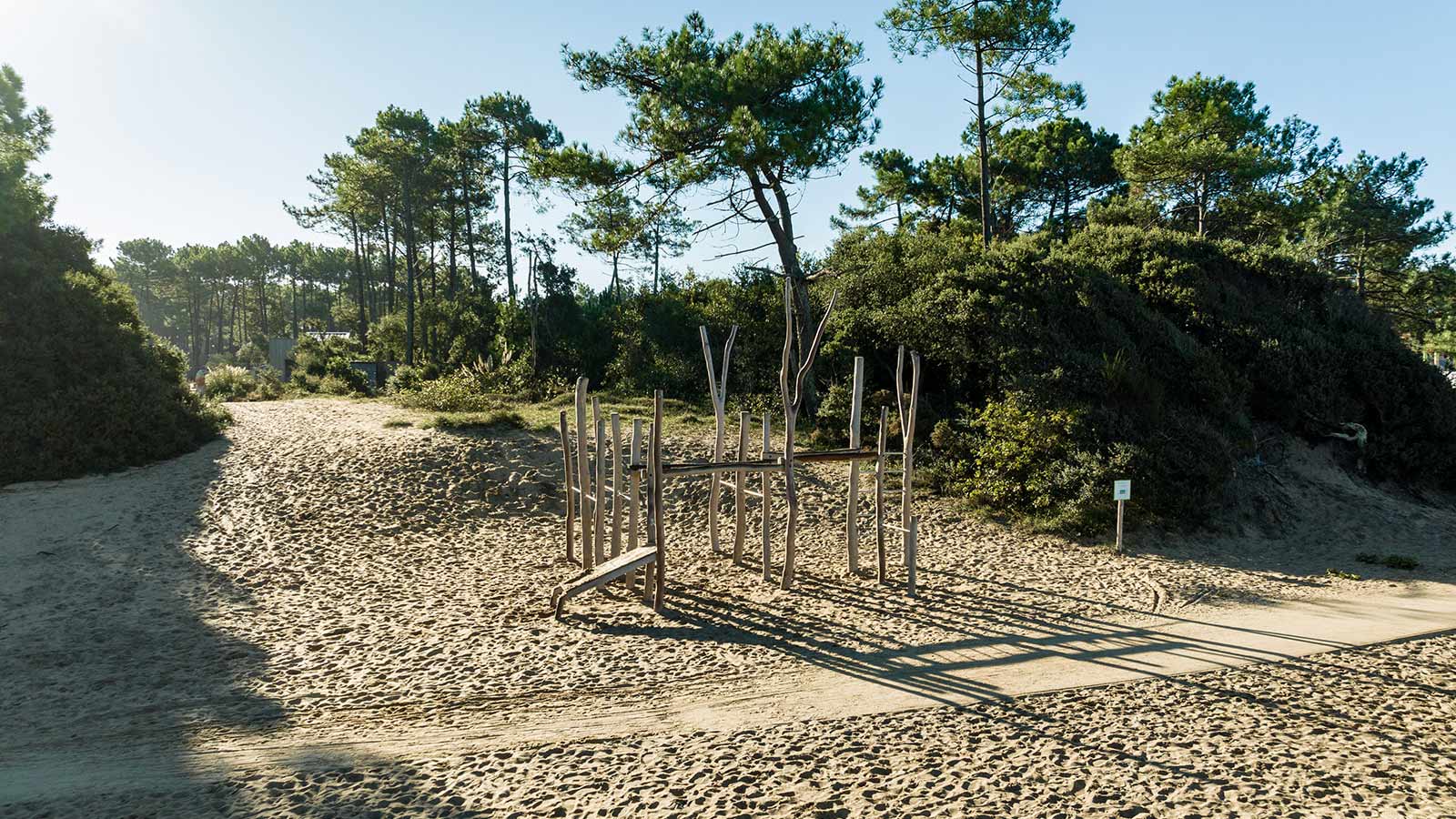 Structure en bois naturel sur une plage de sable fin bordée de pins et de végétation méditerranéenne