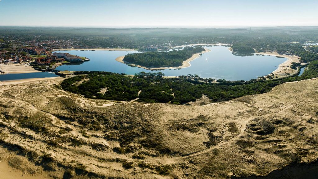Vue aérienne d'un lac entouré de dunes de sable et de forêts de pins près d'une station balnéaire