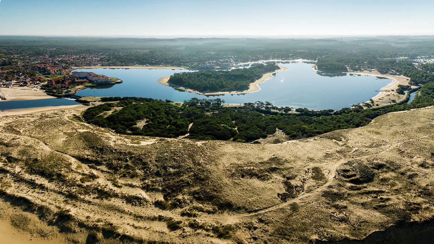 Vue aérienne d'un lac entouré de dunes de sable et de forêts de pins près d'une station balnéaire