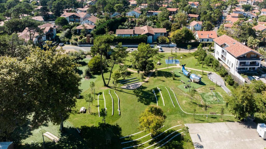 Vue aérienne d'un espace vert urbain avec aire de jeux, pelouse et arbres dans un quartier résidentiel français