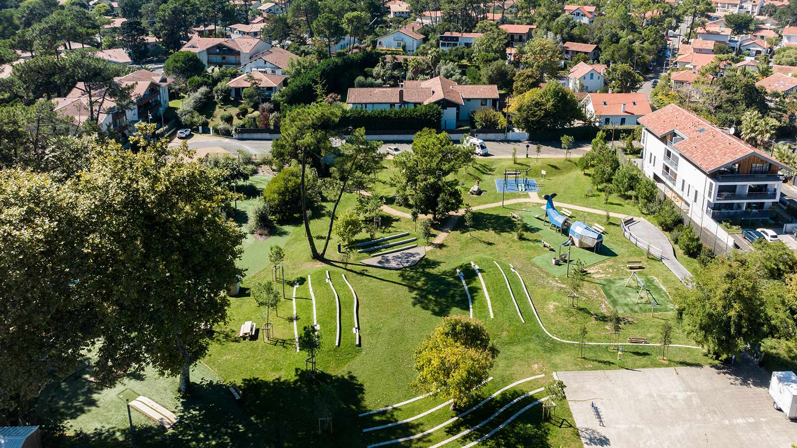 Vue aérienne d'un espace vert urbain avec aire de jeux, pelouse et arbres dans un quartier résidentiel français