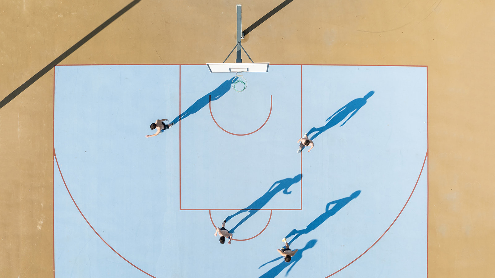 Vue aérienne d'un terrain de basketball bleu avec quatre joueurs et leurs ombres portées au sol