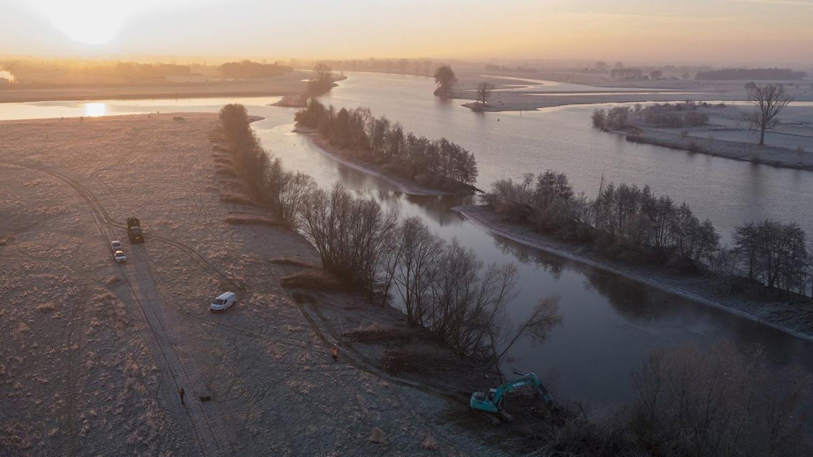 Vue aérienne d'un chantier de terrassement en bord de rivière par un matin d'hiver givré au lever du soleil