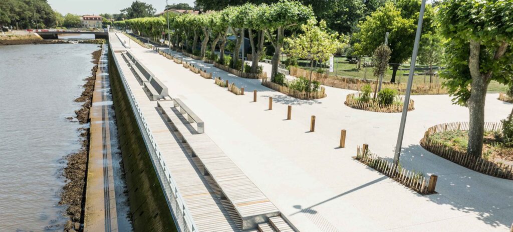 Aménagement paysager d'un quai bordé d'un mail planté, avec esplanade minérale et gradins en bois face à l'eau.