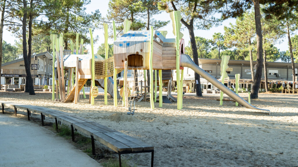 Aire de jeux en bois sous une pinède au sol sableux