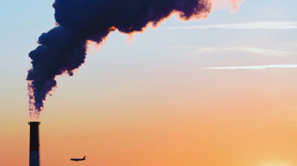 Cheminée industrielle rejetant un panache de fumée au-dessus d'une ville au coucher du soleil
