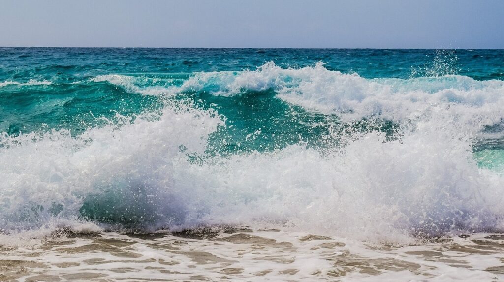 Vague déferlante à l'écume blanche s'échouant sur une plage de sable