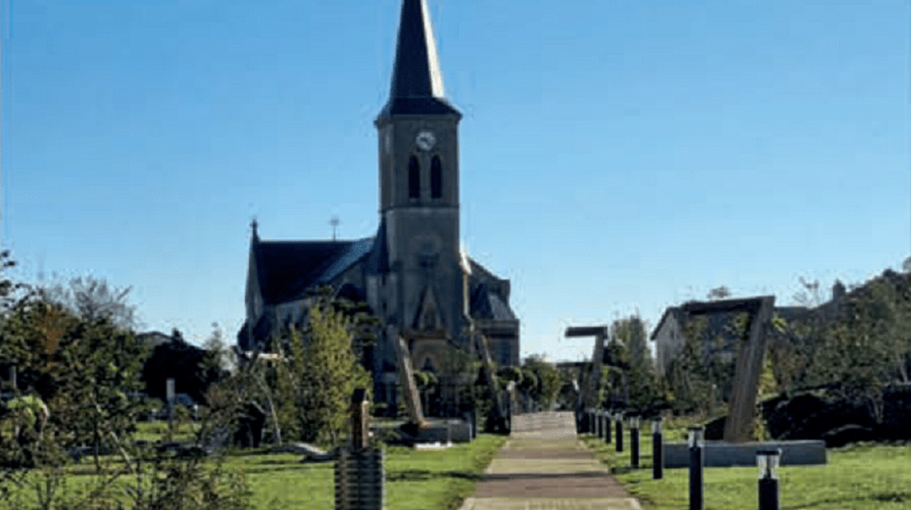 Cimetière paysager avec allée végétalisée menant à une église