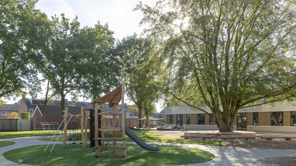 Aire de jeux en bois sur gazon devant un bâtiment scolaire entouré de grands arbres