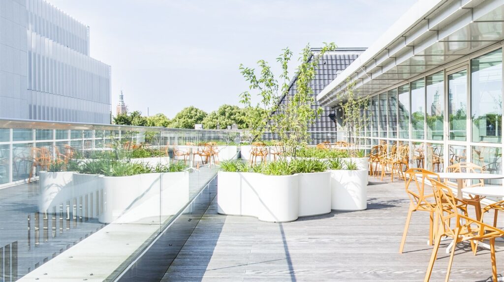 Terrasse de bureaux avec bacs plantés, mobilier en bois et façade vitrée