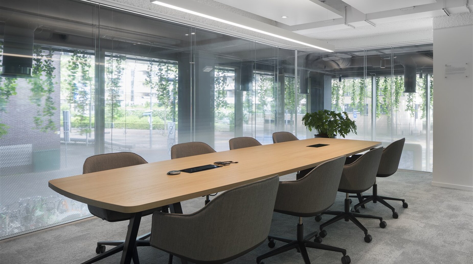 Salle de réunion vitrée avec grande table ovale et plantes devant une baie donnant sur la verdure