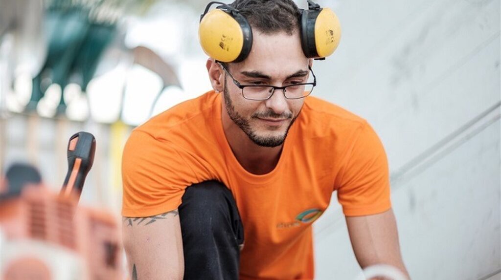 Ouvrier en tee-shirt orange équipé d'un casque antibruit maniant une tronçonneuse