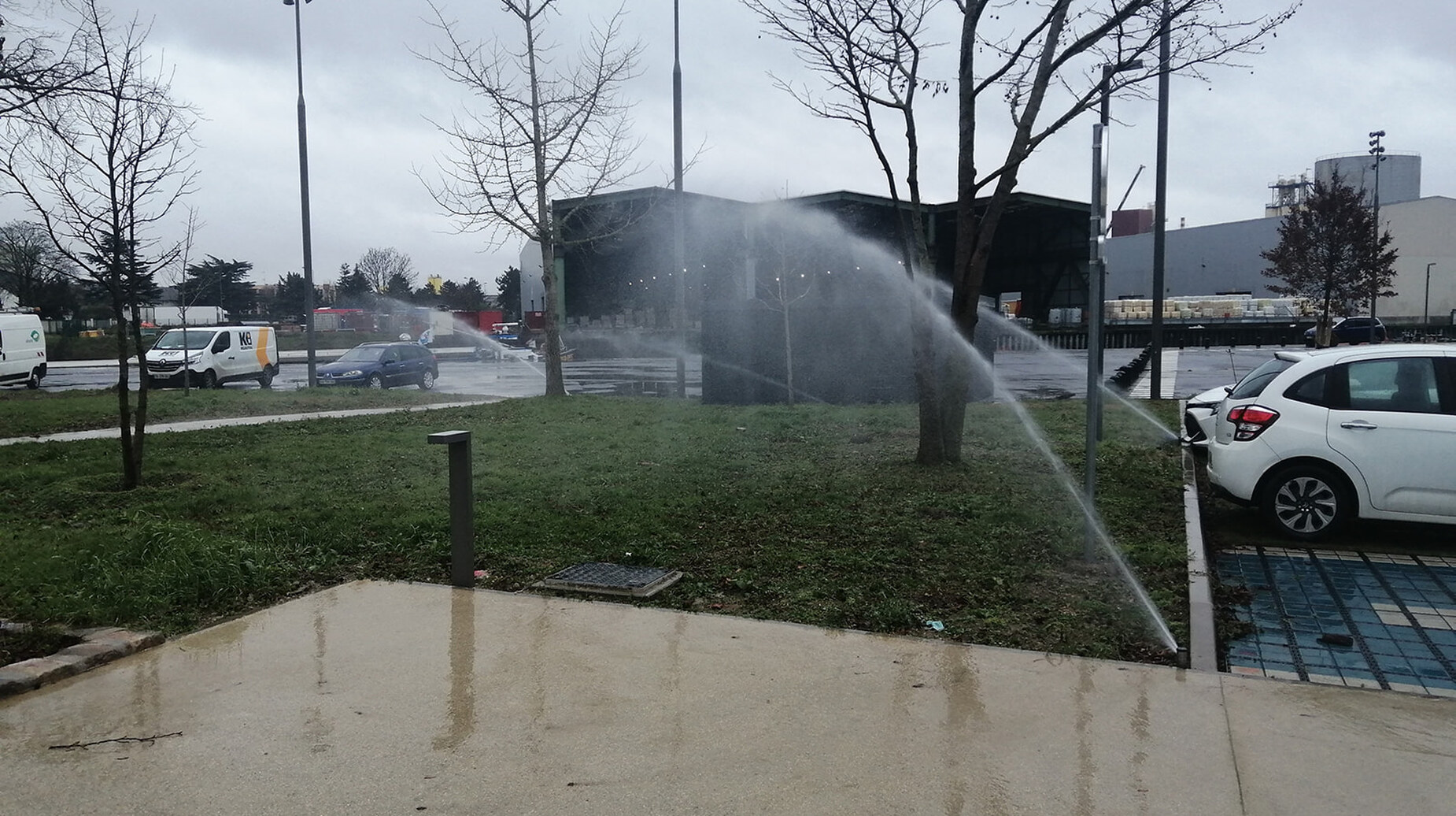 Arrosage d'une pelouse urbaine par asperseurs près d'un parking