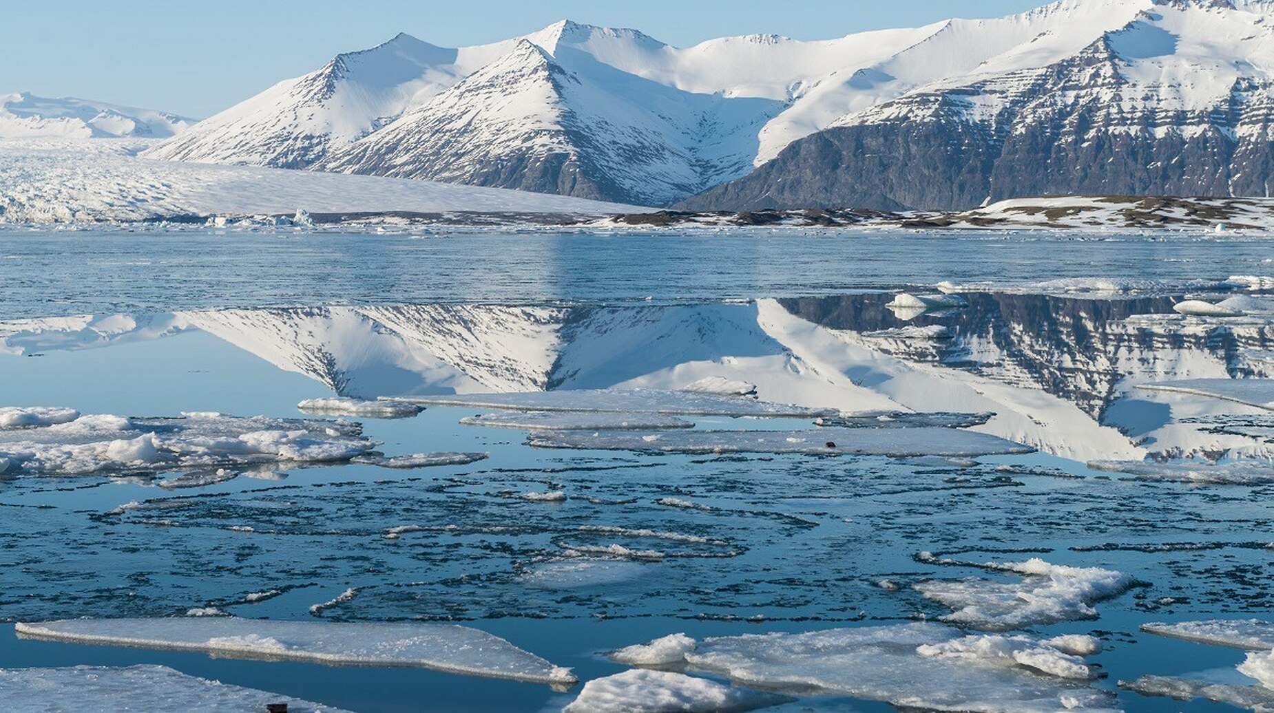 Lagune glaciaire parsemée de blocs de glace devant des montagnes enneigées